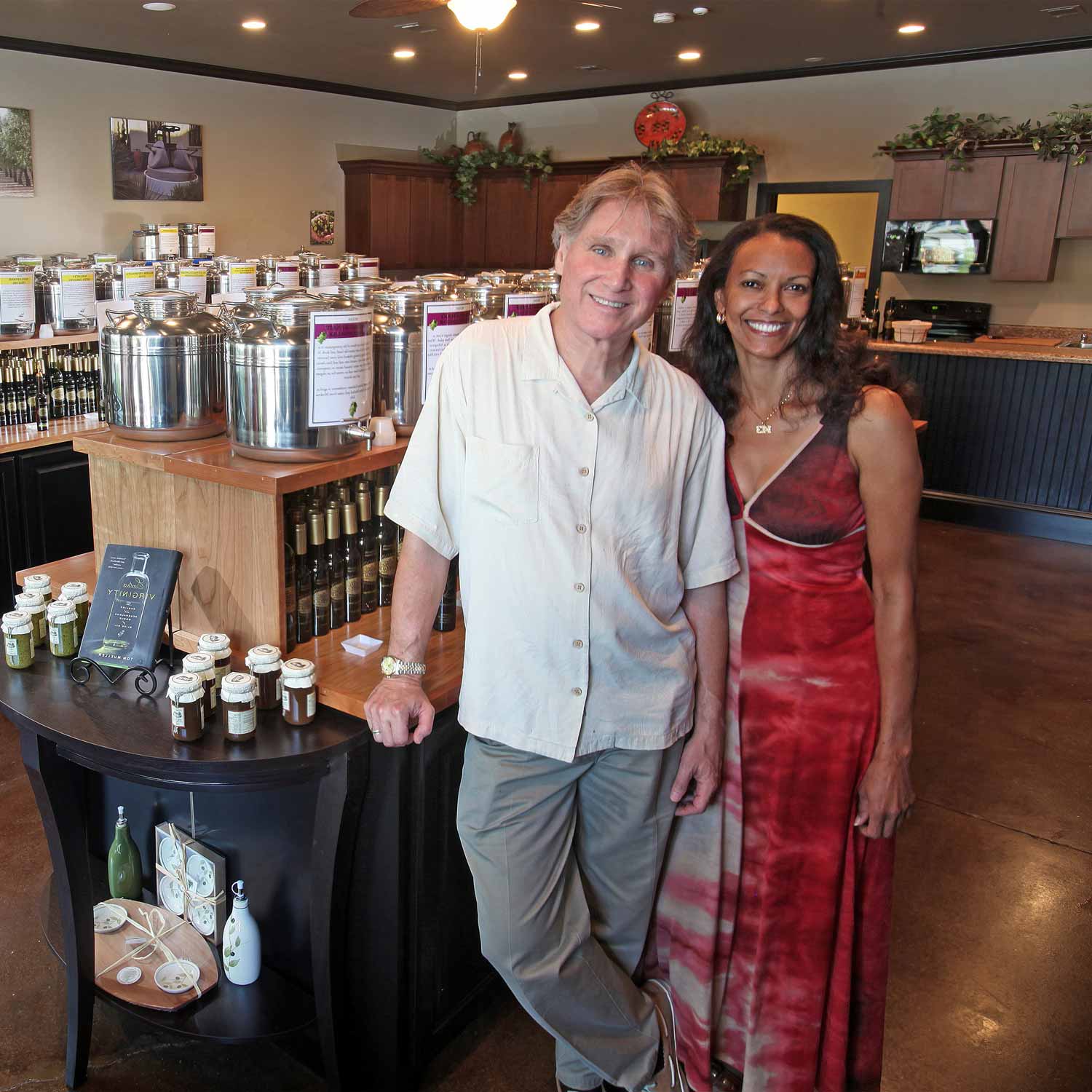 Store owners Larry and Carol Jack smile together standing with olive oil barrels at their lake oconee store.
