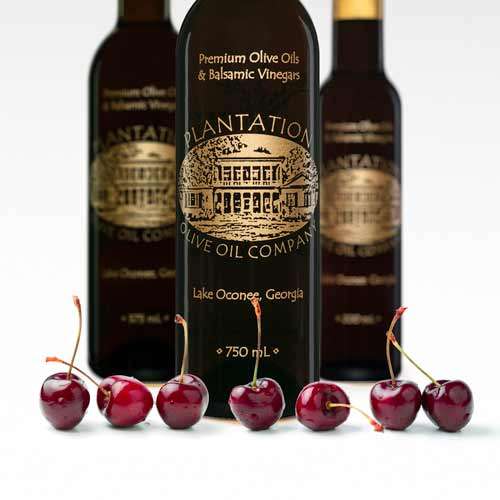 Photo showing a row of fresh picked dark cherries in front of three bottles of dark balsamic vinegar.
