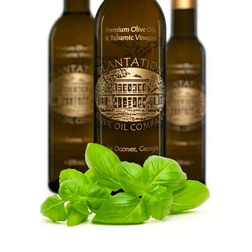 Photo showing a fresh sprig of basil in front of three bottles of olive oil. 