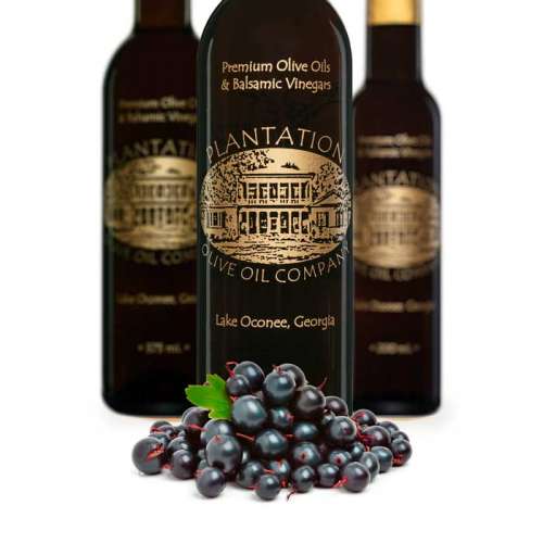 Photo of fresh black currant berries piled in front of three bottles of dark balsamic vinegar.