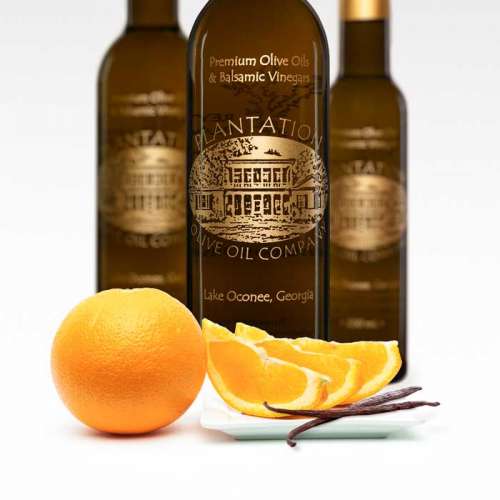 Photo showing a whole Cara Cara orange and slices with two vanilla beans on a dish in front of three bottles of white vinegar