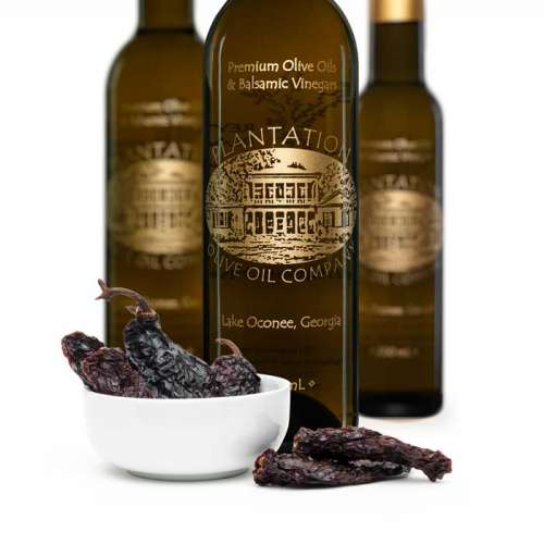 Photo showing chipotle peppers overflowing from small bowl in front of three bottles of olive oil.