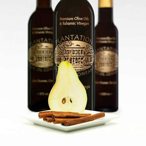 Photo of fresh cut half pear and cinnamon sticks in front of three bottles of dark balsamic vinegar.