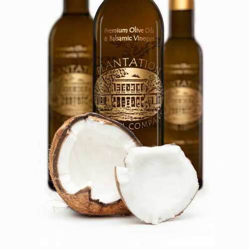 Photo showing a fresh cracked coconut in front of three bottles of white balsamic vinegar.