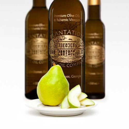 Photo showing Comice pear and pear slice on small plate in front of three bottles of white balsamic vinegar