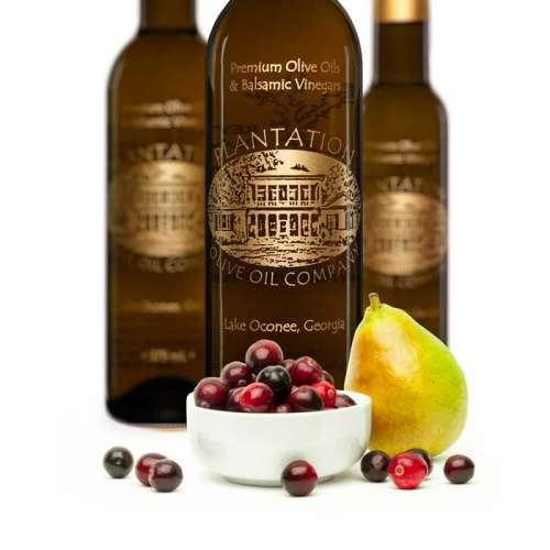 Photo showing small dish of fresh cranberries next to whole pear in front of three bottles of white balsamic vinegar.