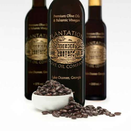 Photo showing fresh espresso coffee beans overflowing from small bowl in front of three bottles of dark balsamic vinegar.