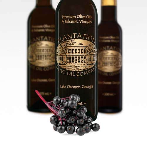 A stem full of elderberries lays in front of three bottles of dark balsamic vinegar on a white background.