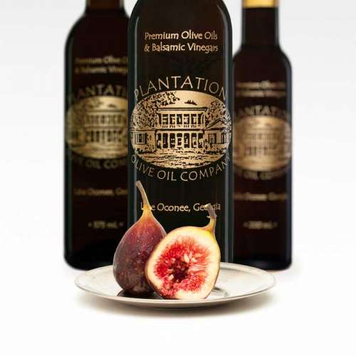 Photo showing fresh whole and cut fig half on a small plate in front of three bottles of dark balsamic vinegar.