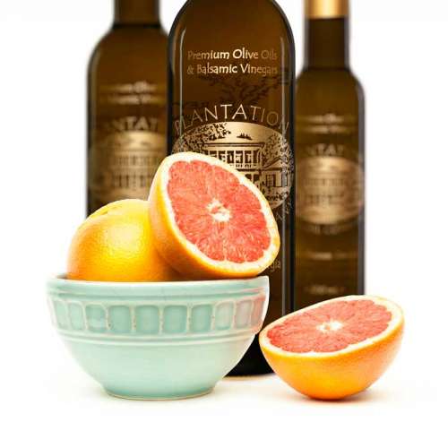 Photo showing a porcelain bowl of fresh whole and cut grapefruit in front of three bottles of white balsamic vinegar.