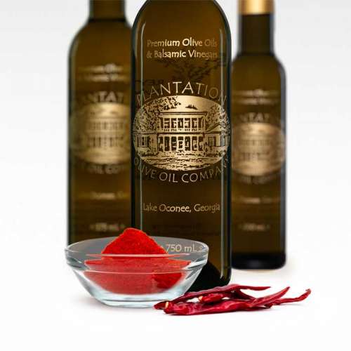 Photo showing fresh ground harissa chili powder in front of three bottles of olive oil.