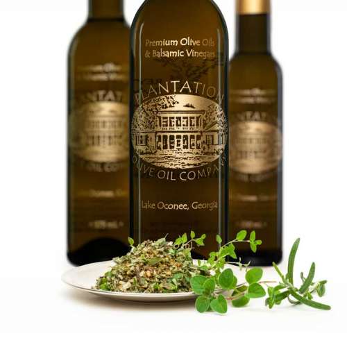 Photo showing fresh cut herbs de Provence and sprig of oregano on small dish in front of three bottles of olive oil