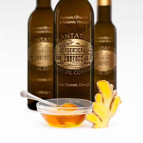 Photo showing a small clear glass bowl of honey with spoon inside and freshly sliced ginger next to the bowl