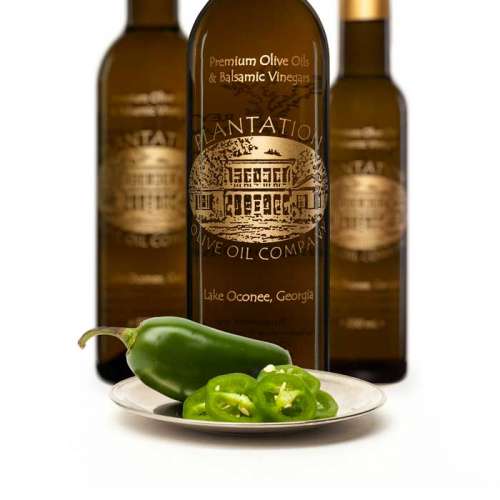Photo showing fresh whole and cut jalopeno peppers on a small plate in front of three bottles of white balsamic vinegar.