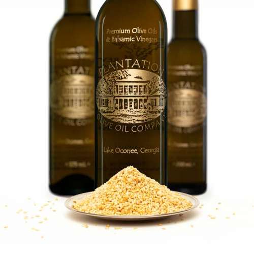 Photo showing roasted sesame seeds in front of three olive oil bottles.