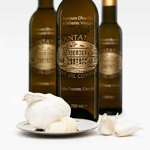 Photo showing fresh whole garlic and garlic cloves in front of three bottles of olive oil.