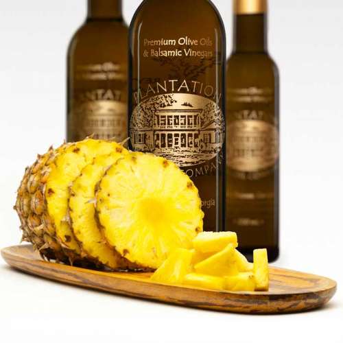 Photo showing whole pineapple slices on a cutting board in front of three bottles of white balsamic vinegar
