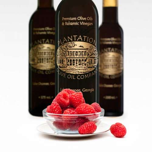 Photo showing fresh raspberries in a small clear glass bowl in front of three bottles of olive oil.