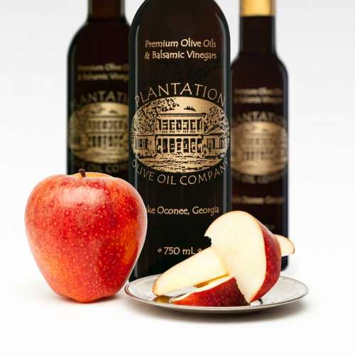 Photo showing whole red apple and red apple slices on small dish in front of three bottles of dark balsamic vinegar.