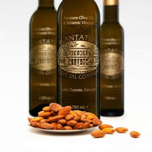 Photo showing whole roasted almonds overflowing from a small plate in front of three bottles of olive oil.