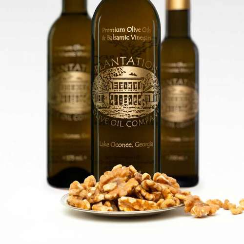 Photo showing small plate of roasted walnuts in front of three bottles of olive oil.