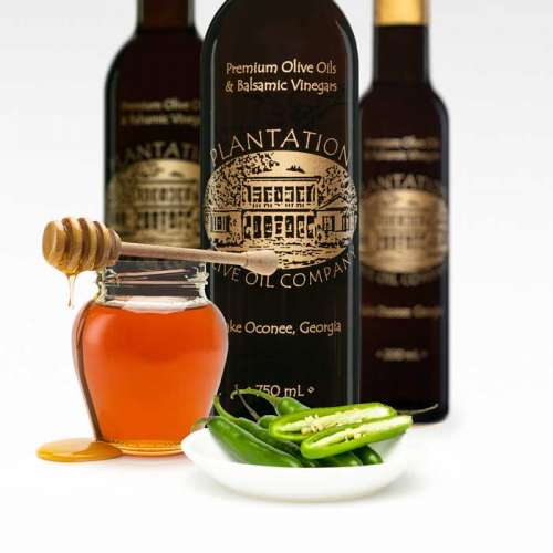 Photo showing jar of honey and dish of sliced Serrano peppers in front of three bottles of dark balsamic vinegar.