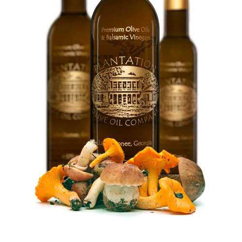 Photo showing piled wild mushrooms in front of three bottles of olive oil.