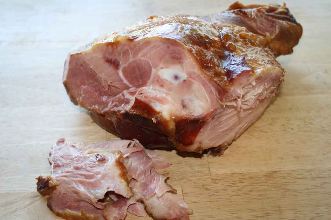 A fresh balsamic glazed ham on a cutting board ready for serving.