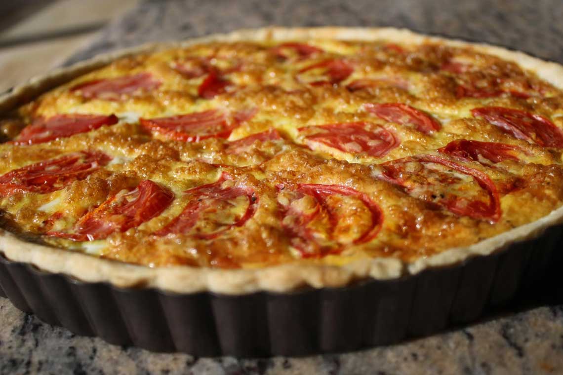 A delicious and fresh tomato quiche in a round pan sitting on topof a kitchen counter.